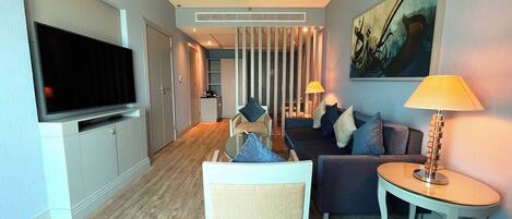 A modern hotel room with a flat-screen TV, a sofa, a chair, a small table, and a lamp.