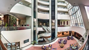 A modern hotel lobby with a central spiral staircase, multiple floors, and a seating area with purple sofas. - Sofitel Al Khobar The Corniche (Al Khobar)