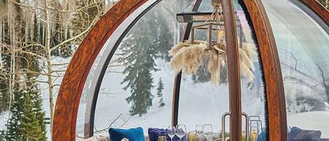 A cozy, circular wooden structure with a glass dome, furnished with a sofa, a table, and two lanterns.