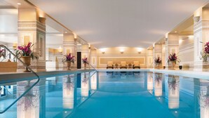 A large indoor swimming pool with a clear blue water surface, surrounded by columns and potted plants.