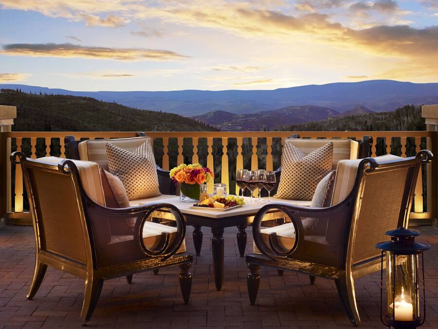 A terrace with a table set for two, featuring a vase of flowers, wine glasses, and a candle.