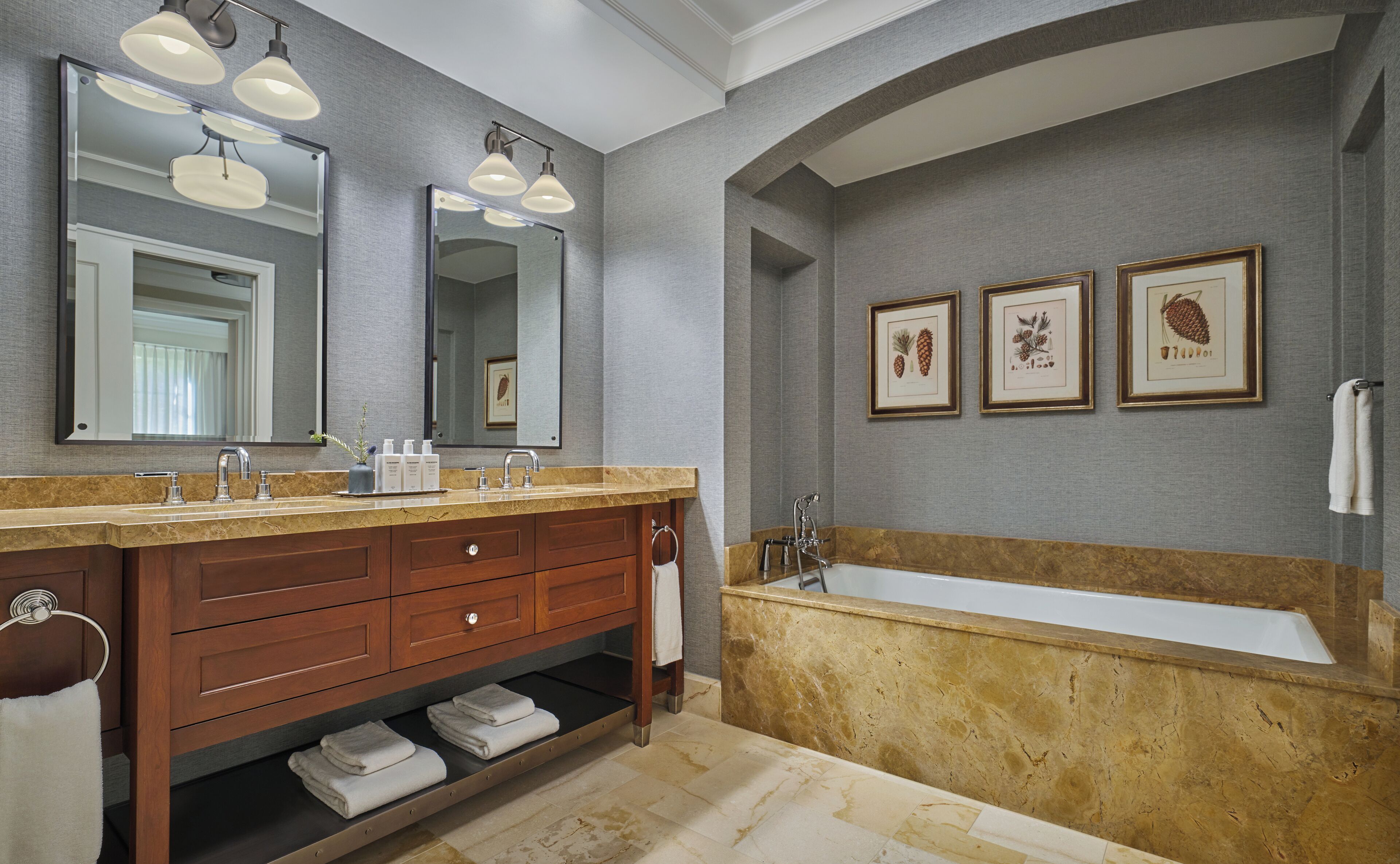 A bathroom with a double vanity, a large bathtub, and three framed botanical prints on the wall.