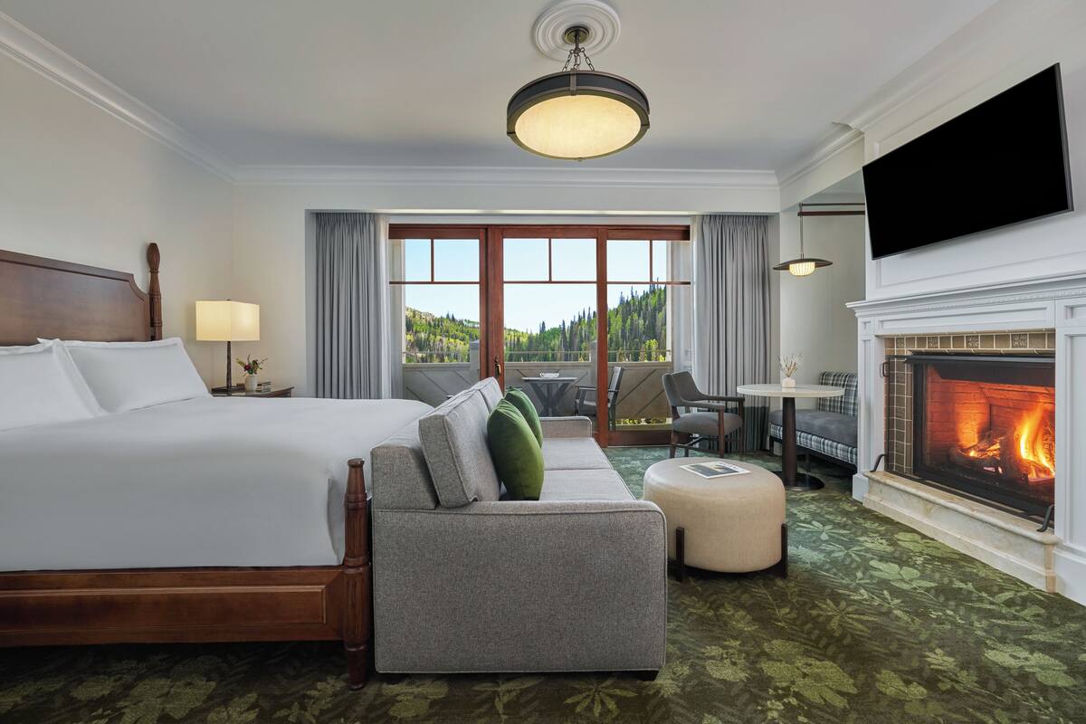 Une chambre d’hôtel avec un grand lit, un canapé, une cheminée et une vue sur l’extérieur.