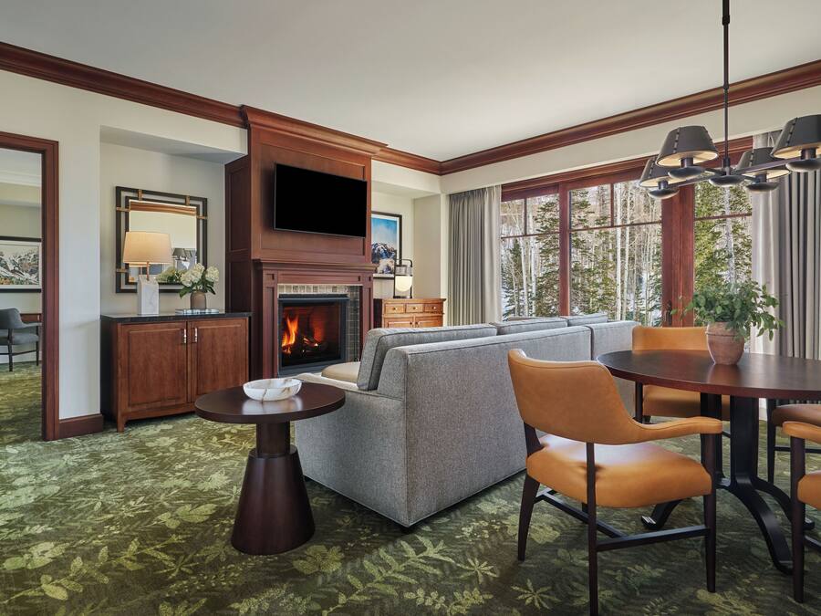 A hotel room with a fireplace, a sofa, a dining table, and a TV.