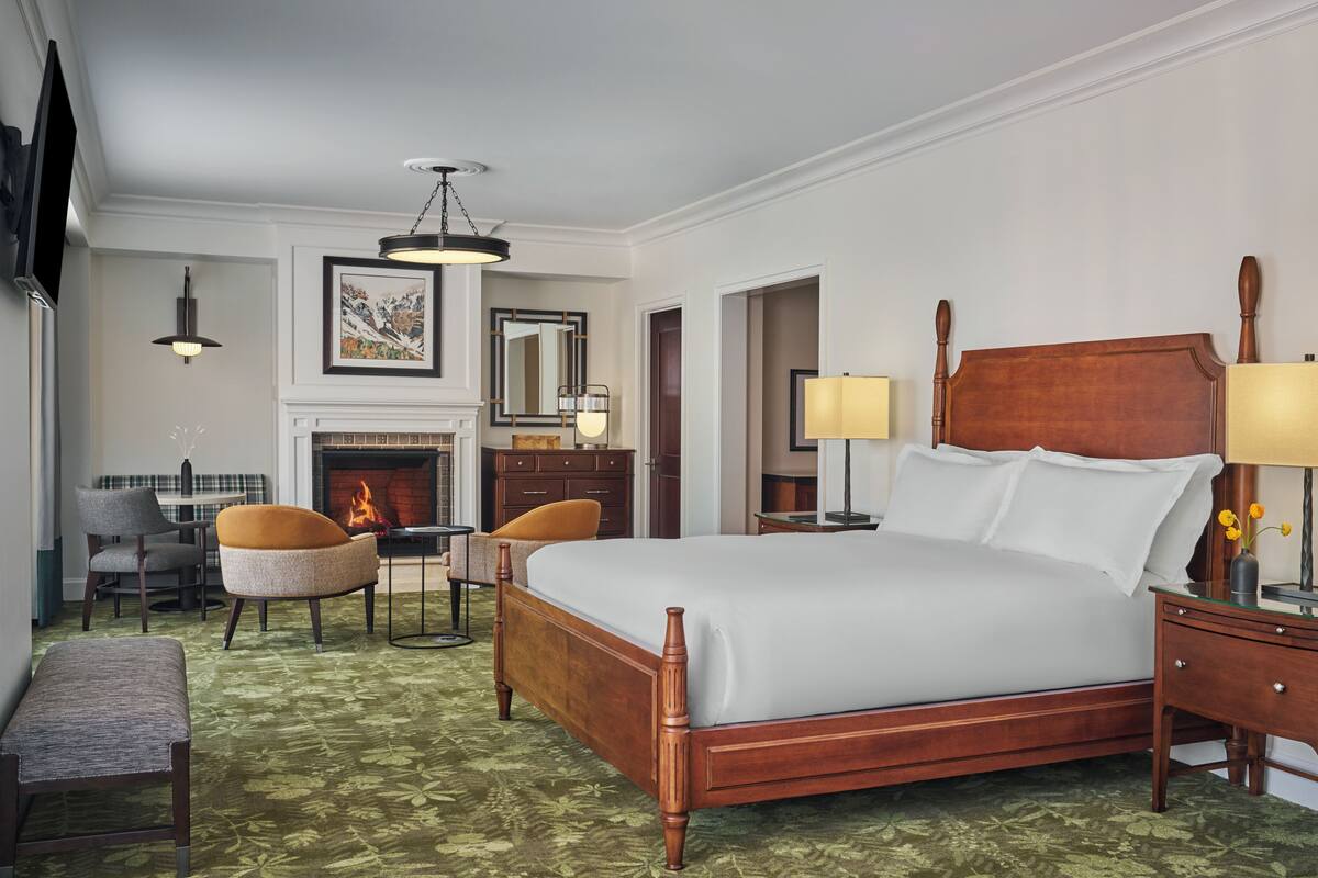 Une chambre d’hôtel dotée d’un grand lit, d’une cheminée, d’un coin repas et d’un espace salon avec des fauteuils.