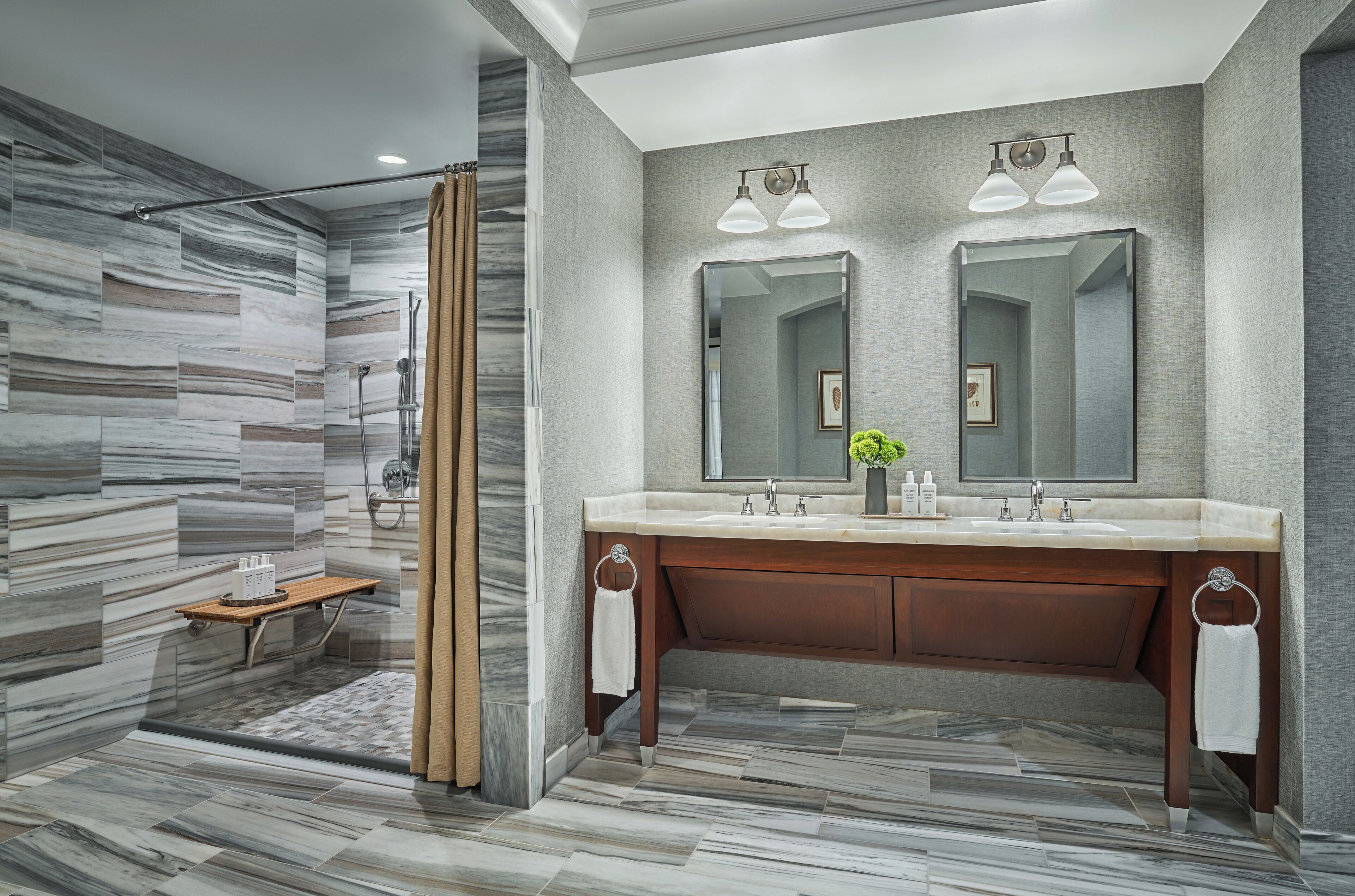 Un baño moderno con ducha de mármol, tocador de madera y espejos dobles.