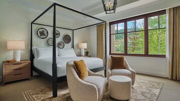 A four-poster canopy bed with a nightstand, two armchairs, and a large window with a view of greenery.