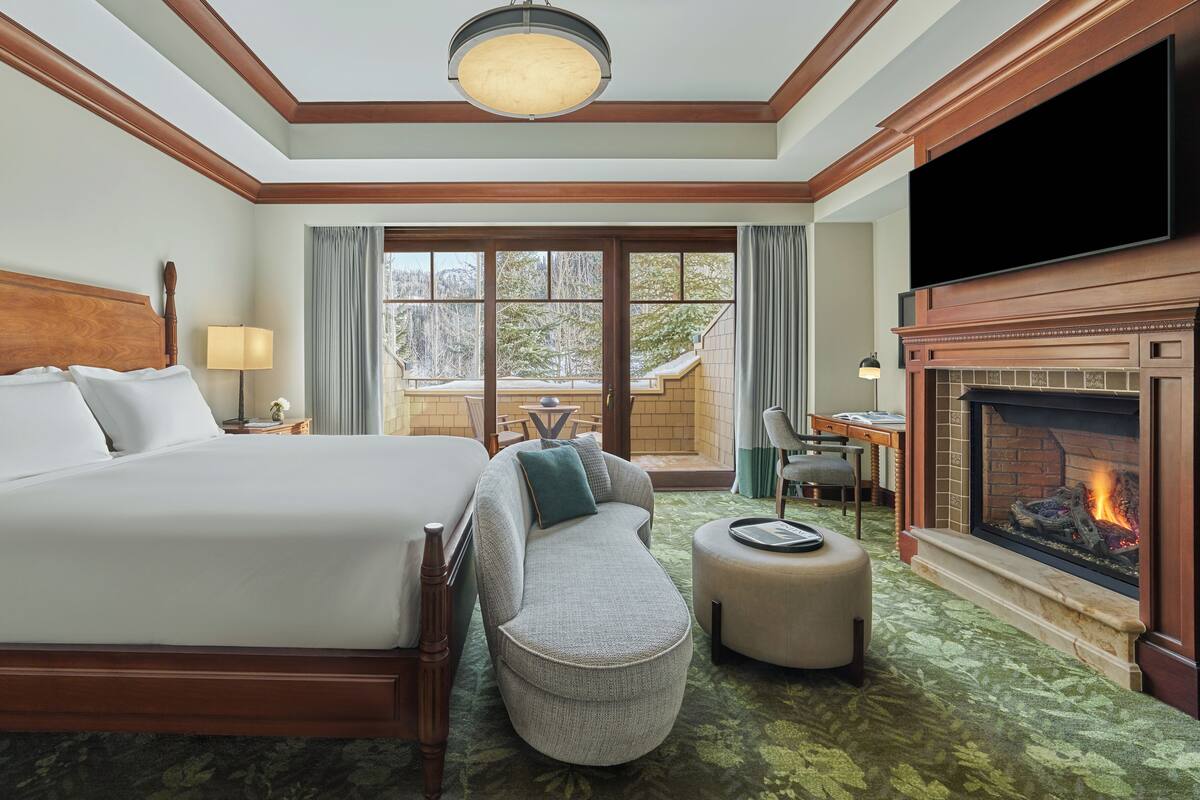 Une chambre d’hôtel dotée d’un grand lit, d’un coin salon, d’une cheminée et offrant une vue sur l’extérieur.