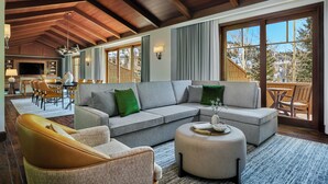 A spacious living area with a large sectional sofa, a round ottoman, and a dining area with a table and chairs.