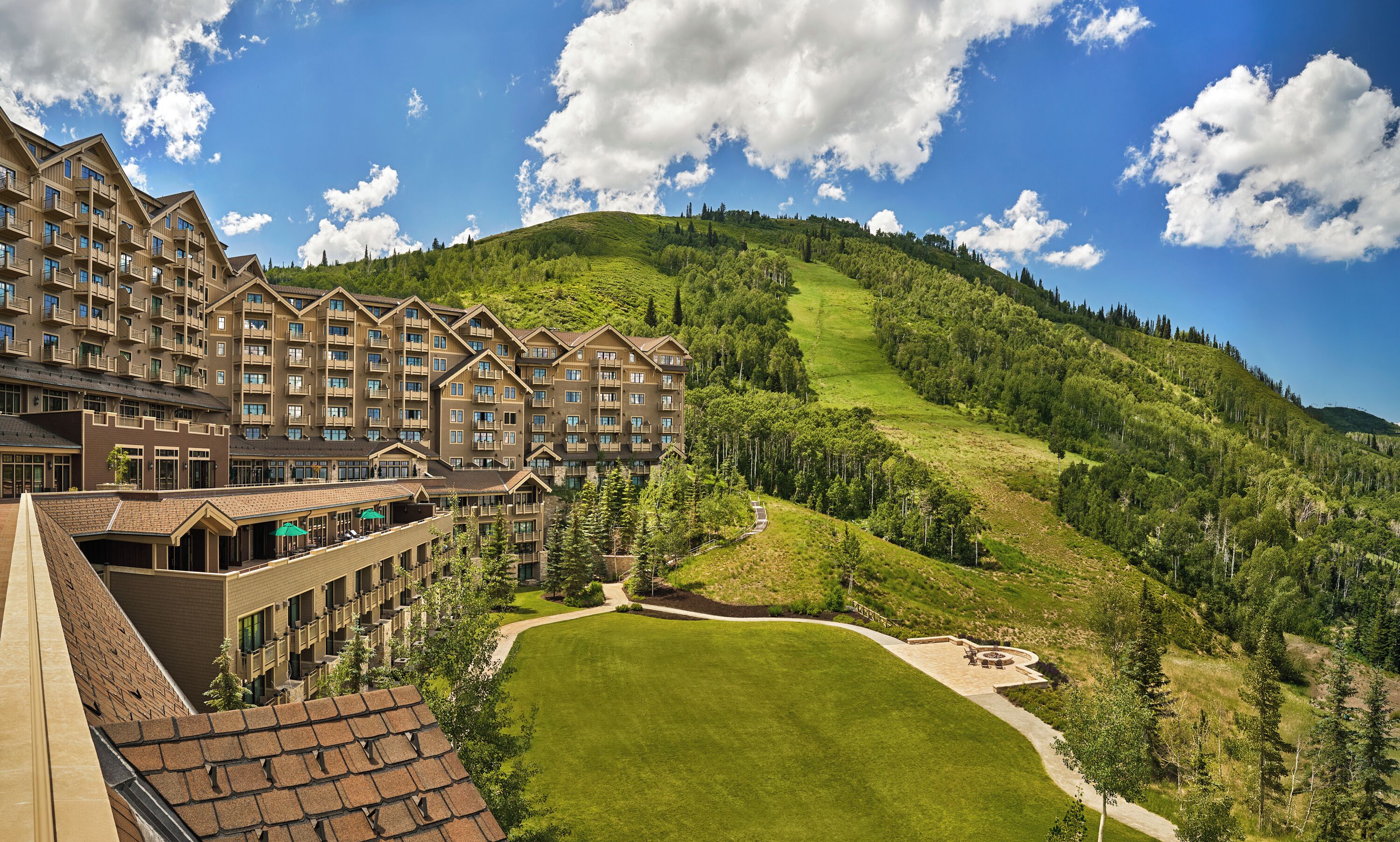 Un hôtel à plusieurs étages doté de balcons, d’une pelouse bien entretenue et surplombant un paysage montagneux.
