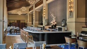 A modern bar area with a long counter, multiple seating arrangements, and decorative lighting fixtures.
