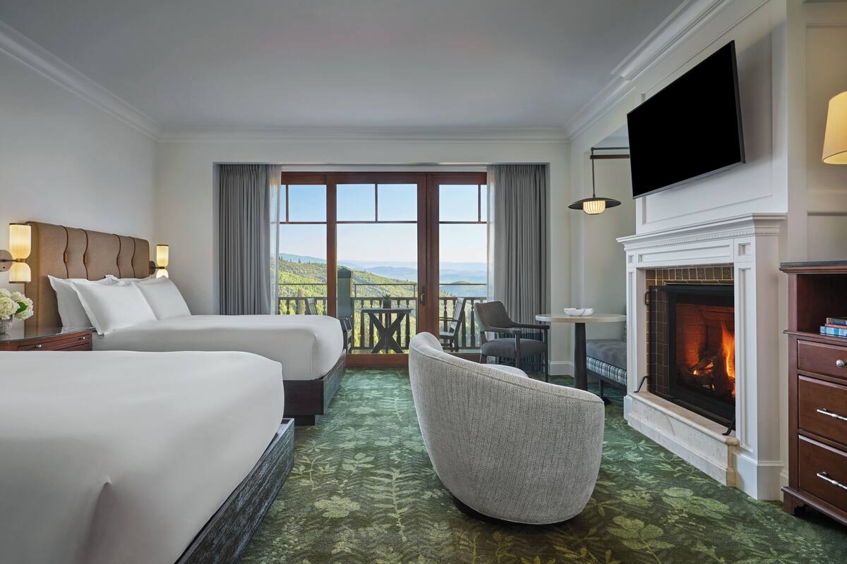 Une chambre d’hôtel avec deux lits, une cheminée, une télévision et un balcon avec vue.