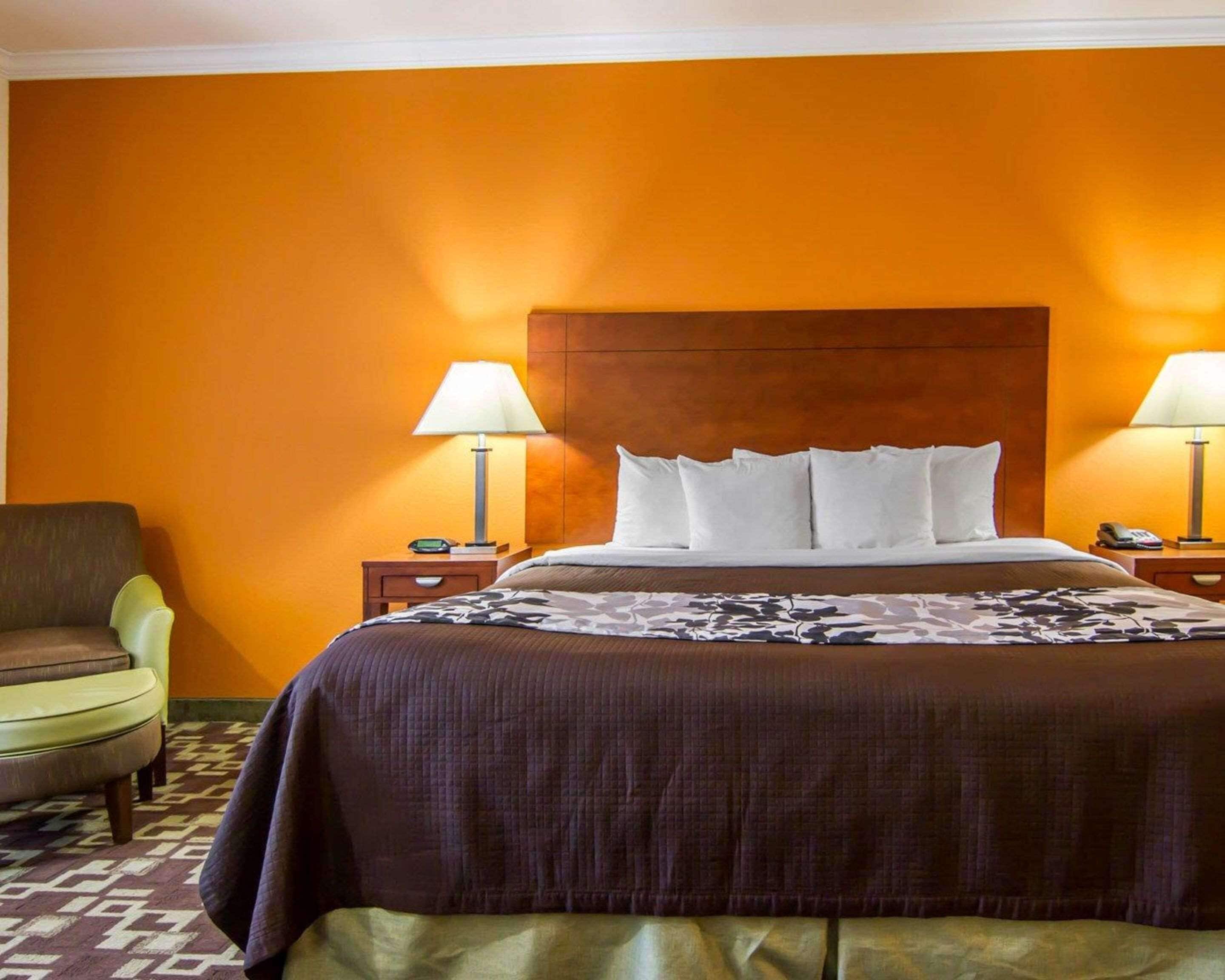 A hotel room with a large bed, two bedside tables with lamps, a chair, and a patterned carpet.