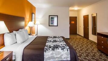 Una habitación de hotel con cama, mesitas de noche, lámpara, un cuadro en la pared y alfombra estampada.