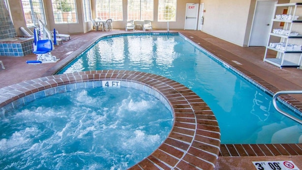 Una gran piscina coberta amb un banyera d'hidromassatge, envoltada per finestres i una zona de seients.
