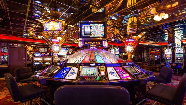 Een speelruimte in een casino met meerdere gokkasten en een centraal scherm.
