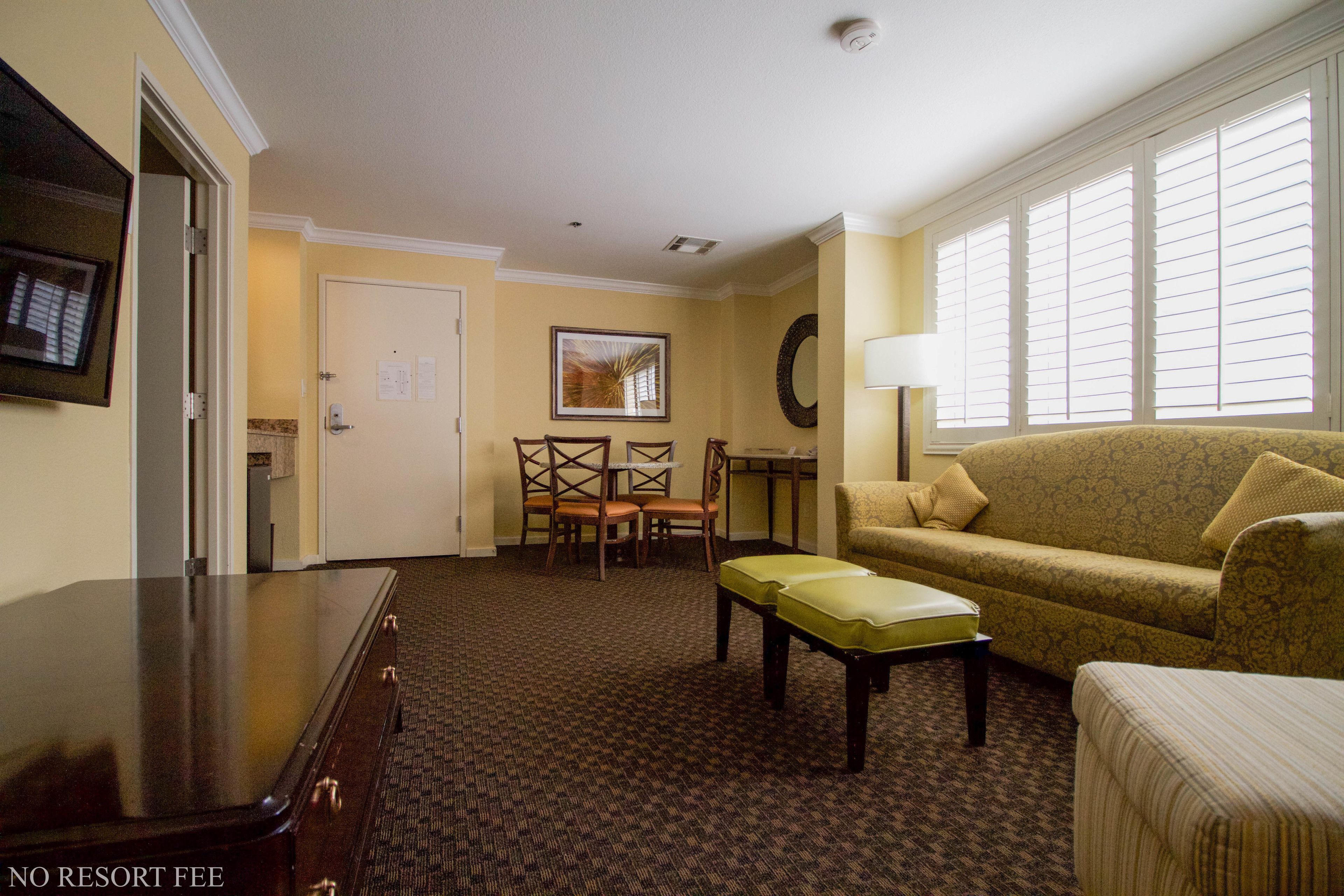 A hotel room with a sofa, a small table, a chair, a bench, a lamp, and a TV.