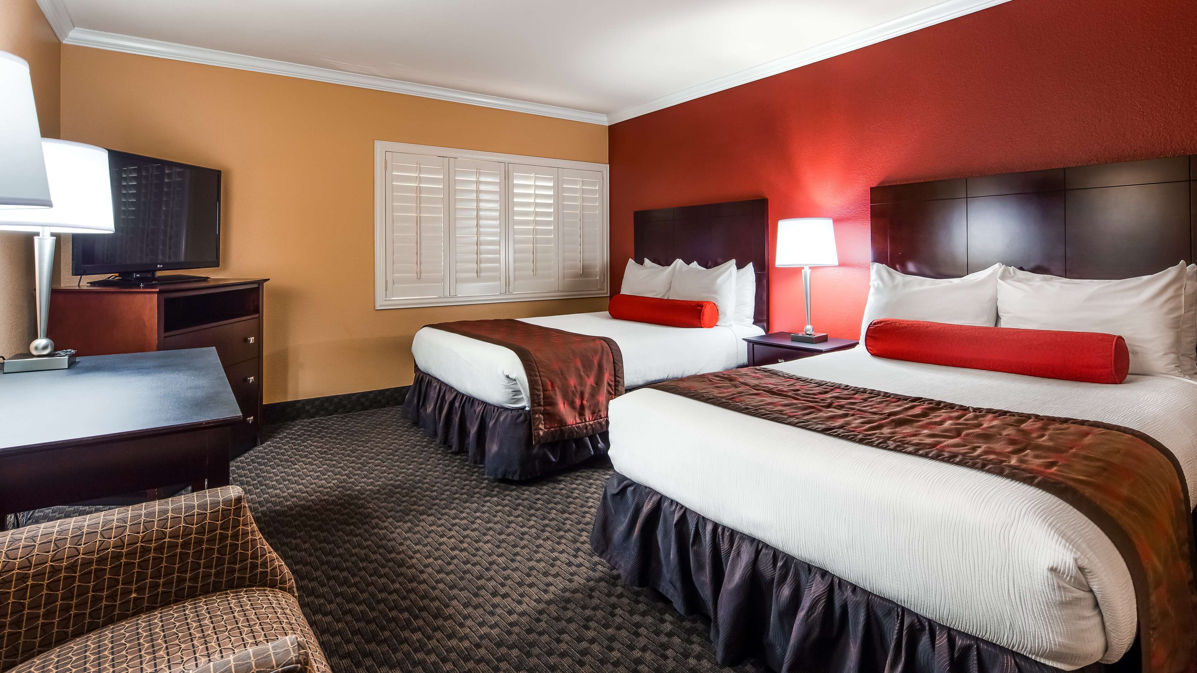 A hotel room with two beds, a desk, a TV, and a window with blinds.