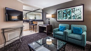 Een hotelkamer met een zithoek, een televisie, een lijst met kunstwerk en een kitchenette.