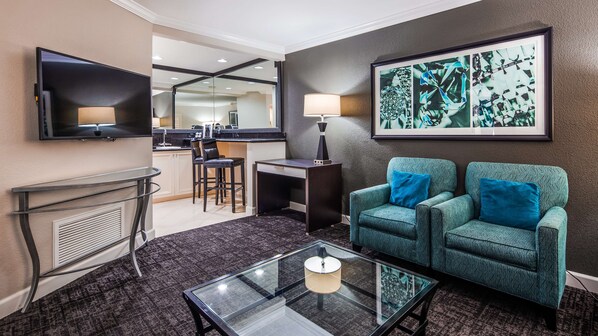 Habitación de hotel con zona de estar, televisor, una obra de arte enmarcada y kitchenette.