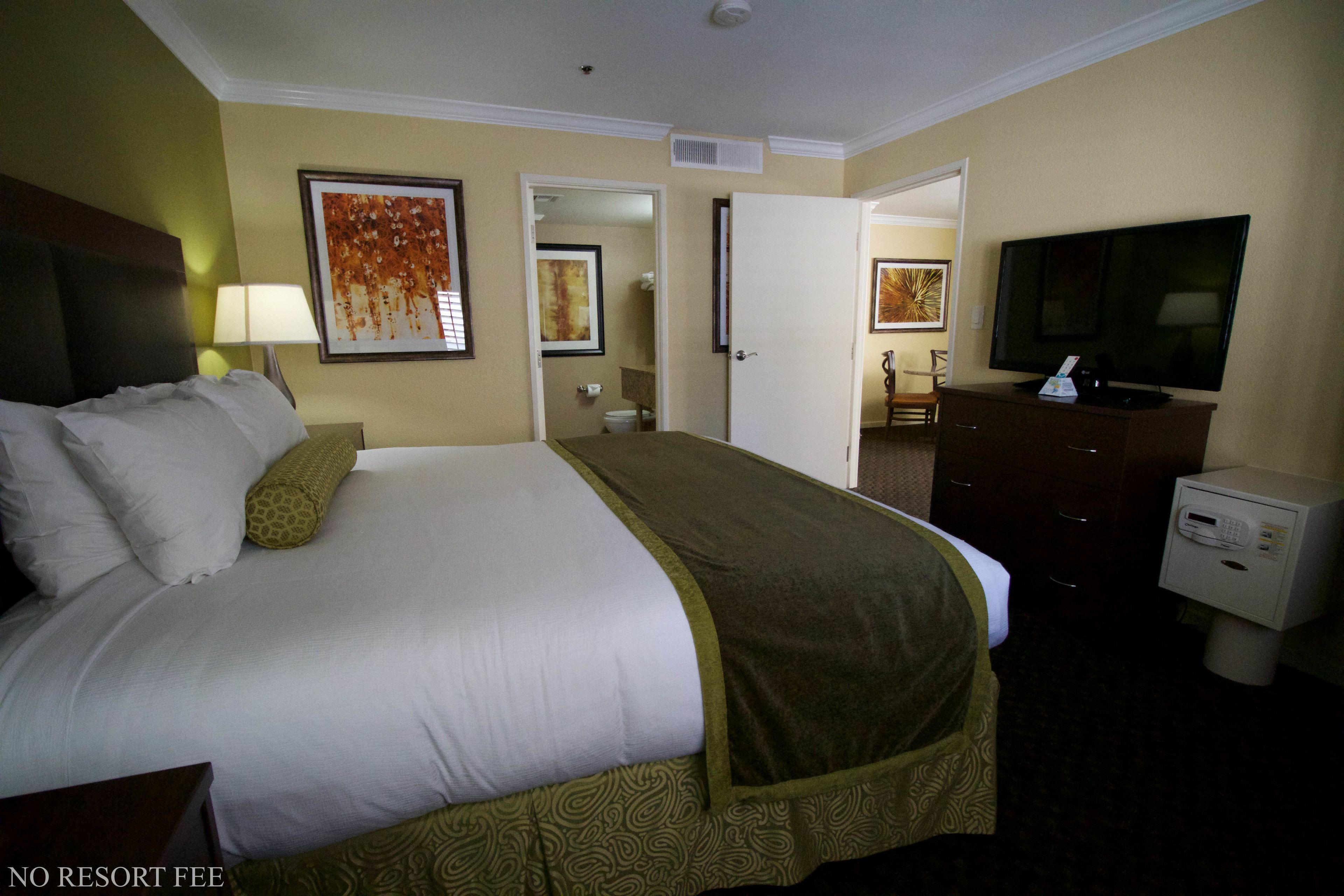 Une chambre d’hôtel avec un grand lit, une télévision, une commode et une salle de bain visible à travers une porte ouverte.