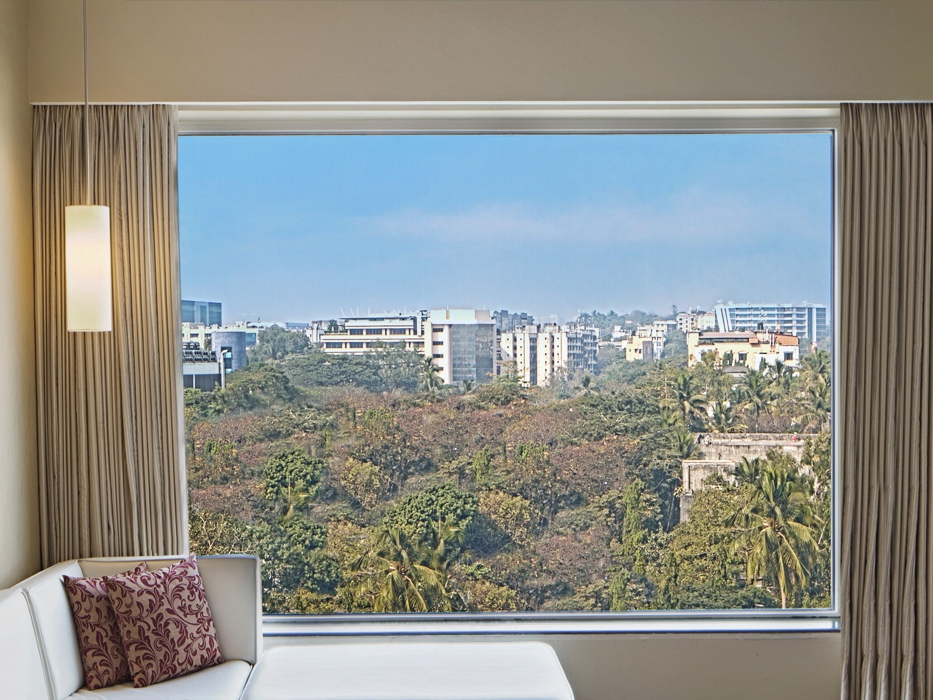 A hotel room with a large window, a sofa, and a view of a cityscape and greenery.