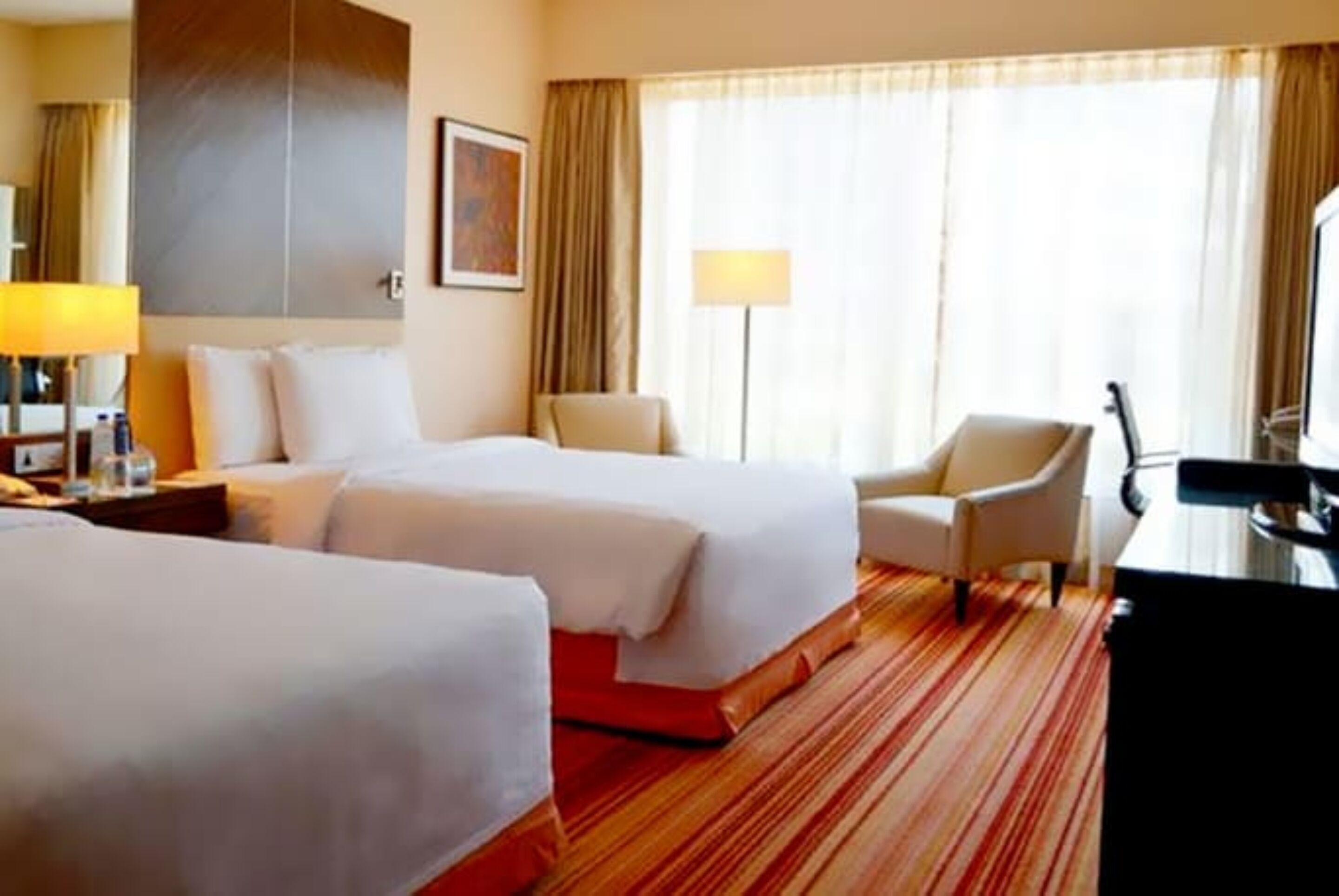 Een hotelkamer met twee bedden, een bureau, een stoel en een groot raam met gordijnen.