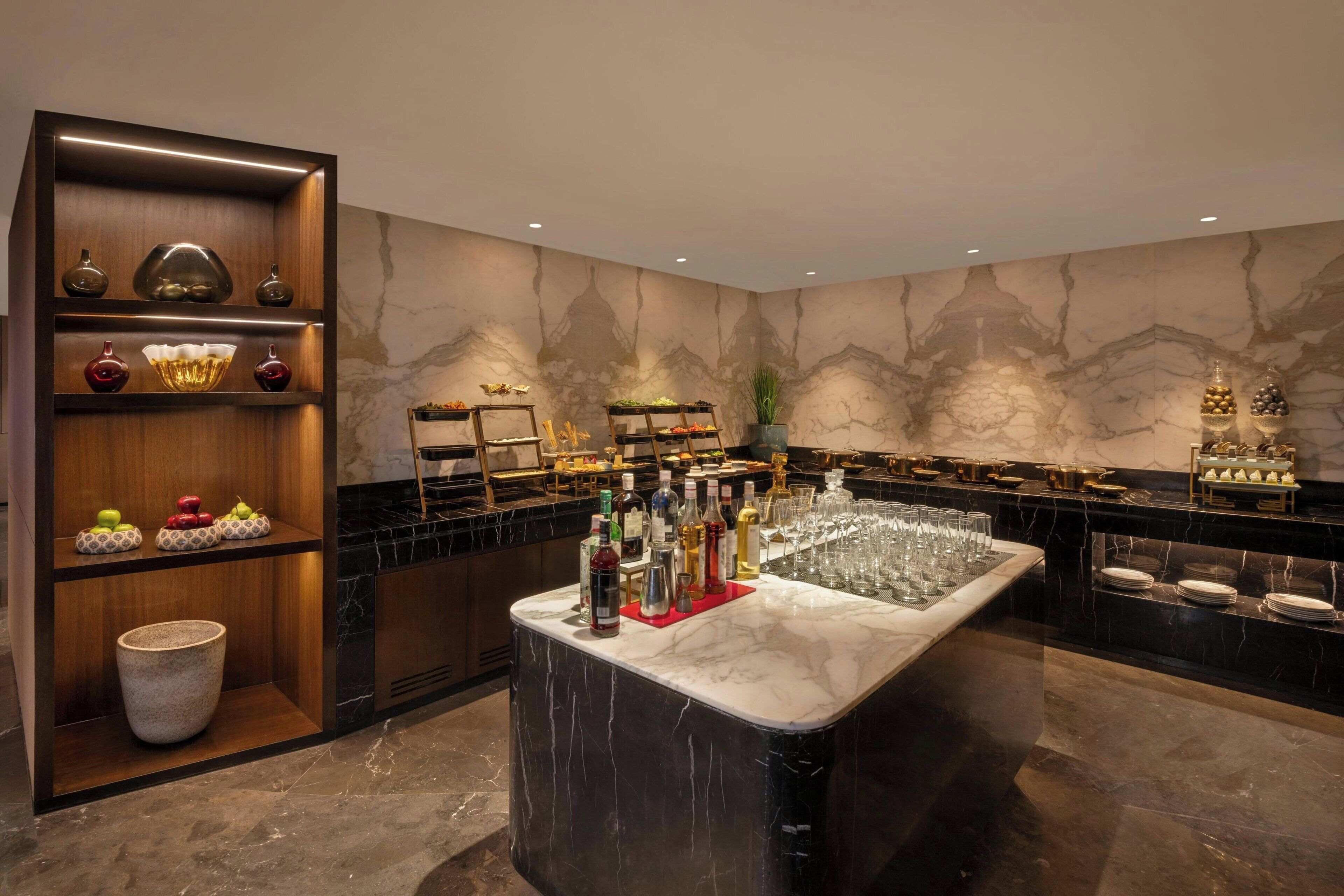 Zona de bar con encimera de mármol, estantes con botellas, vasos y objetos decorativos.