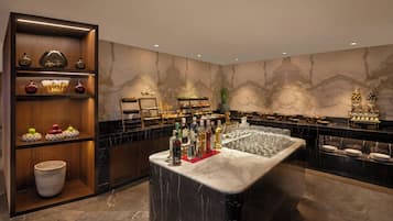 Zona de bar con encimera de mármol, estantes con botellas, vasos y objetos decorativos.