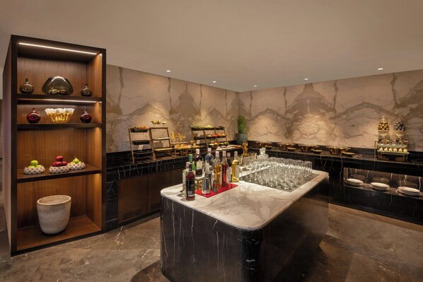 Zona de bar con encimera de mármol, estantes con botellas, vasos y objetos decorativos.