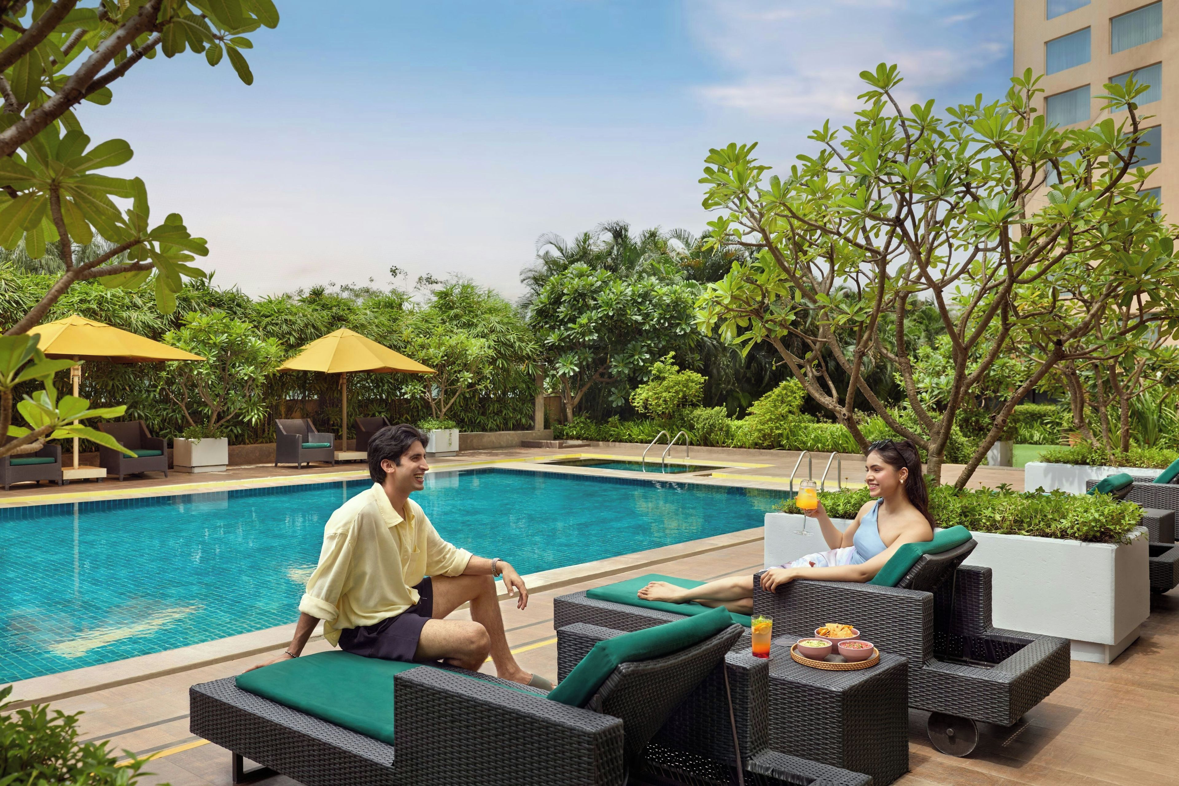 A poolside area with lounge chairs and umbrellas, surrounded by greenery.