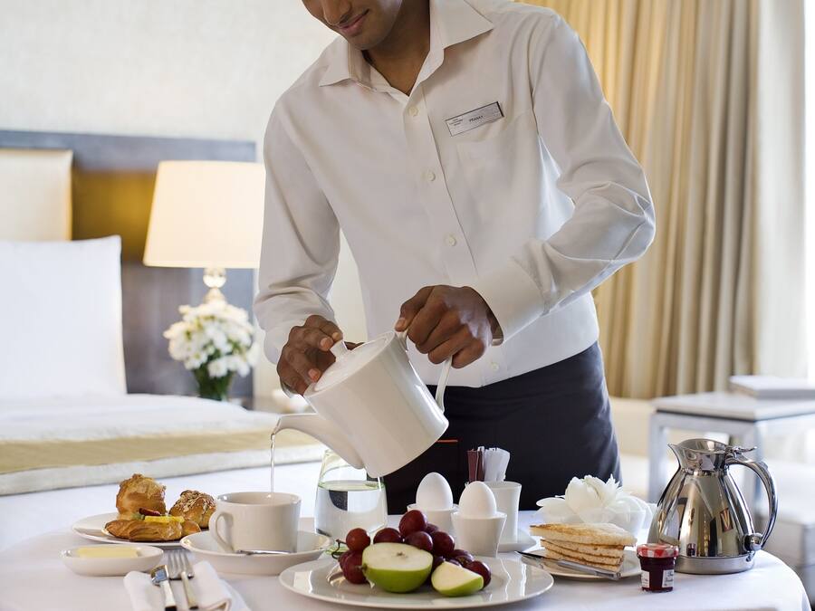 A hotel room with a neatly arranged breakfast table featuring croissants, fruit, and a coffee pot.