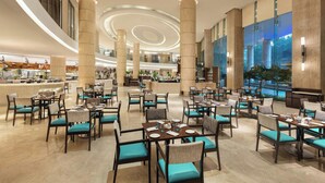 A spacious hotel lobby with multiple dining areas, large pillars, and a view of the outdoors. - Courtyard by Marriott Mumbai International Airport (Mumbai)