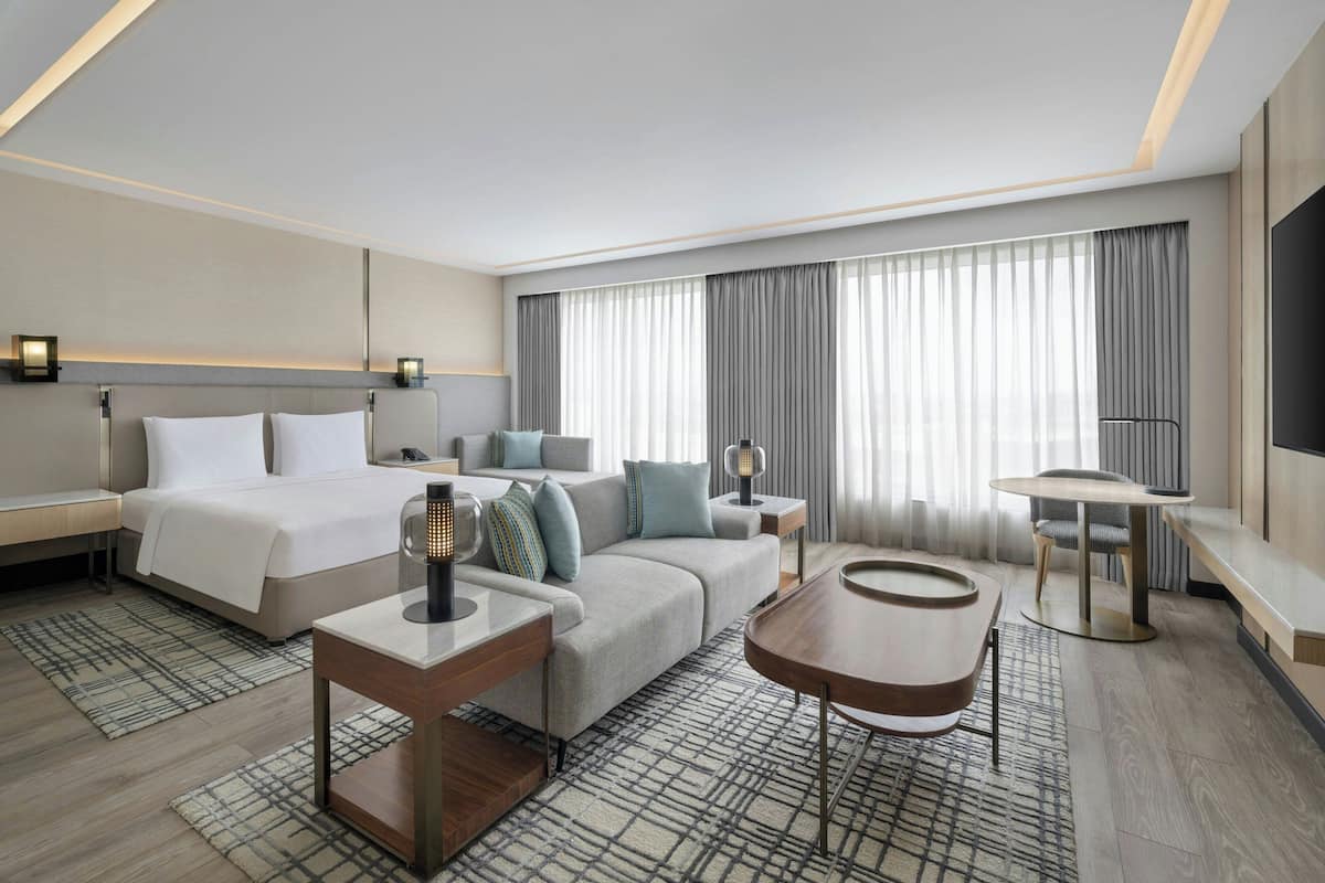 A modern hotel room with a bed, sofa, coffee table, and a dining area.