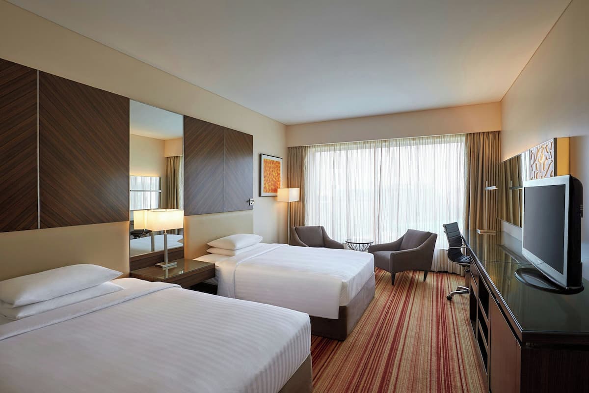 A hotel room with two beds, a desk, a television, and a seating area.