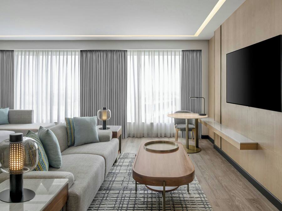 A modern hotel room with a large bed, a sofa, a coffee table, a TV, and a fireplace.