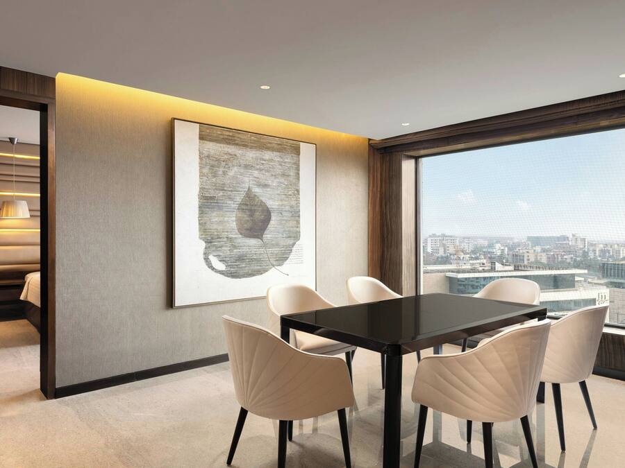 Un comedor moderno con una mesa negra y sillas blancas, un cuadro abstracto grande en la pared y vistas de la ciudad a través de amplios ventanales.