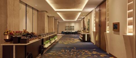 A hotel corridor with a central bar, decorative carpet, and a seating area in the distance.