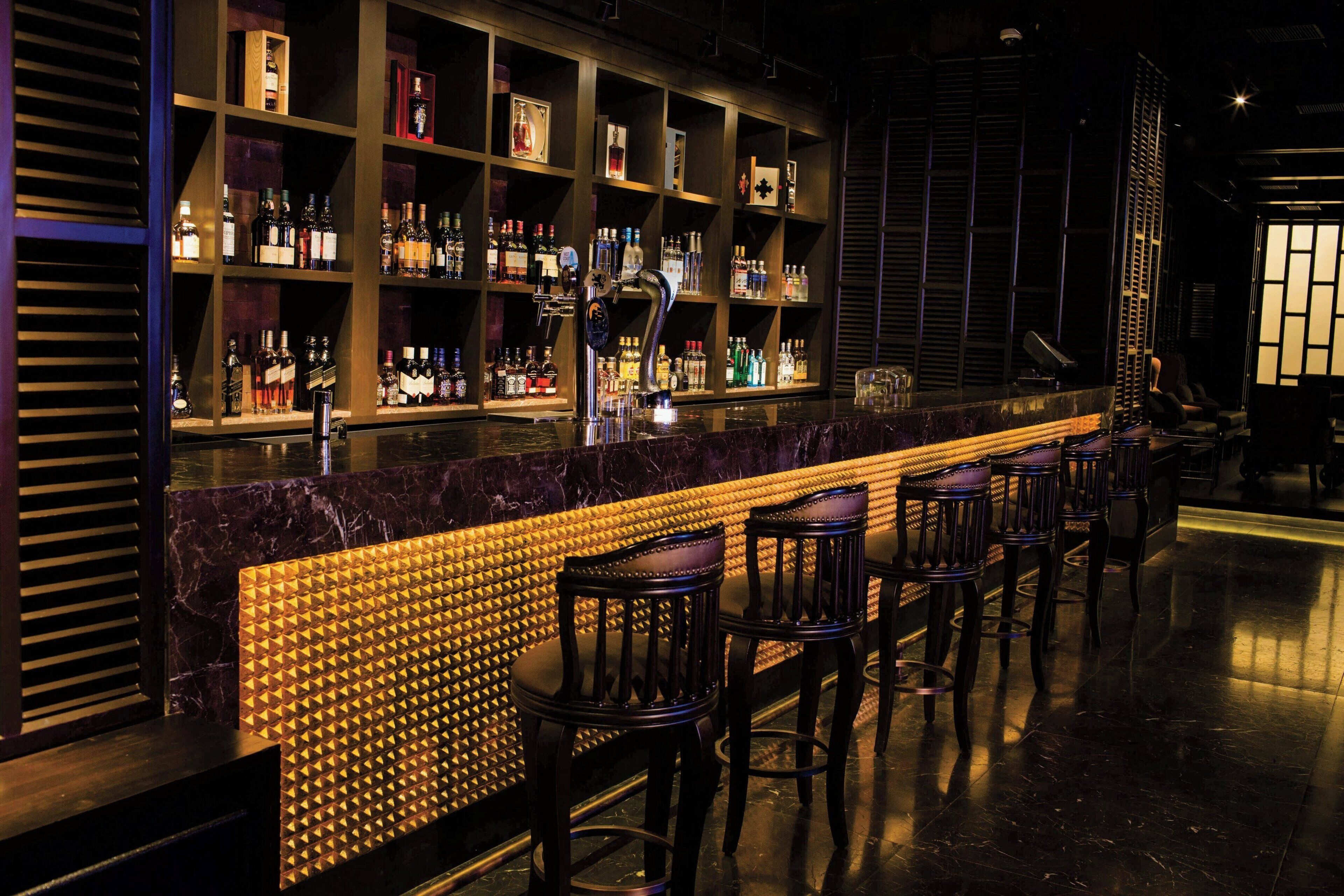 A bar area with a long counter, multiple shelves of bottles, and several bar stools.