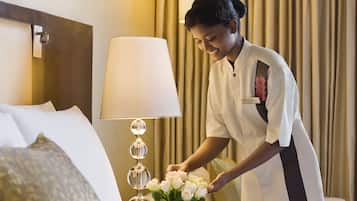 A hotel room with a neatly made bed, a lamp, and a vase of flowers.