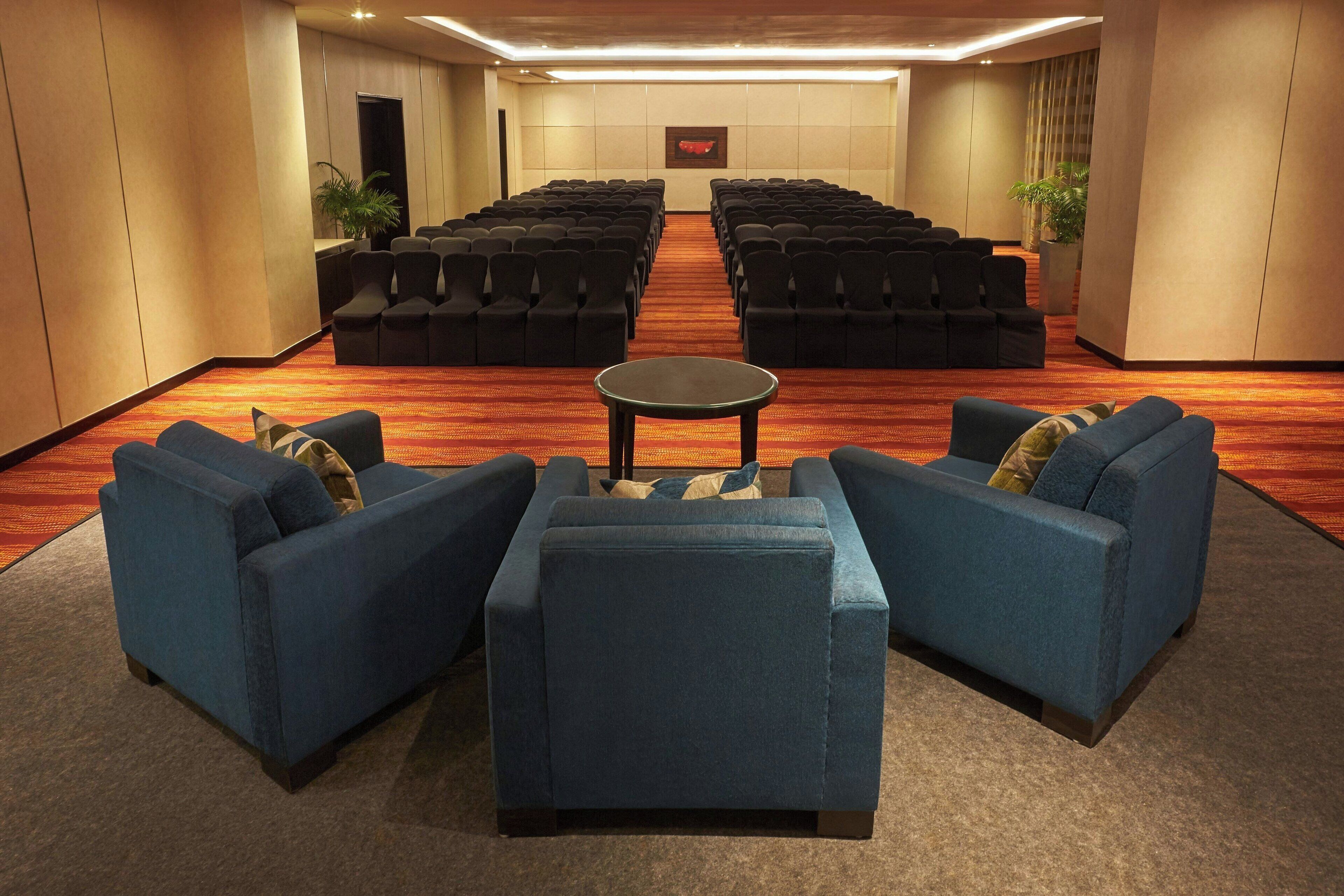 A conference room with rows of black chairs, a central table, and blue sofas with pillows.