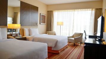 A hotel room with two beds, a desk, a chair, and a TV.