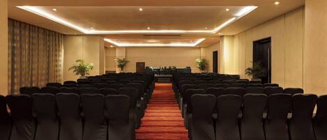A conference room with rows of black chairs, a red carpet, and ceiling lights.