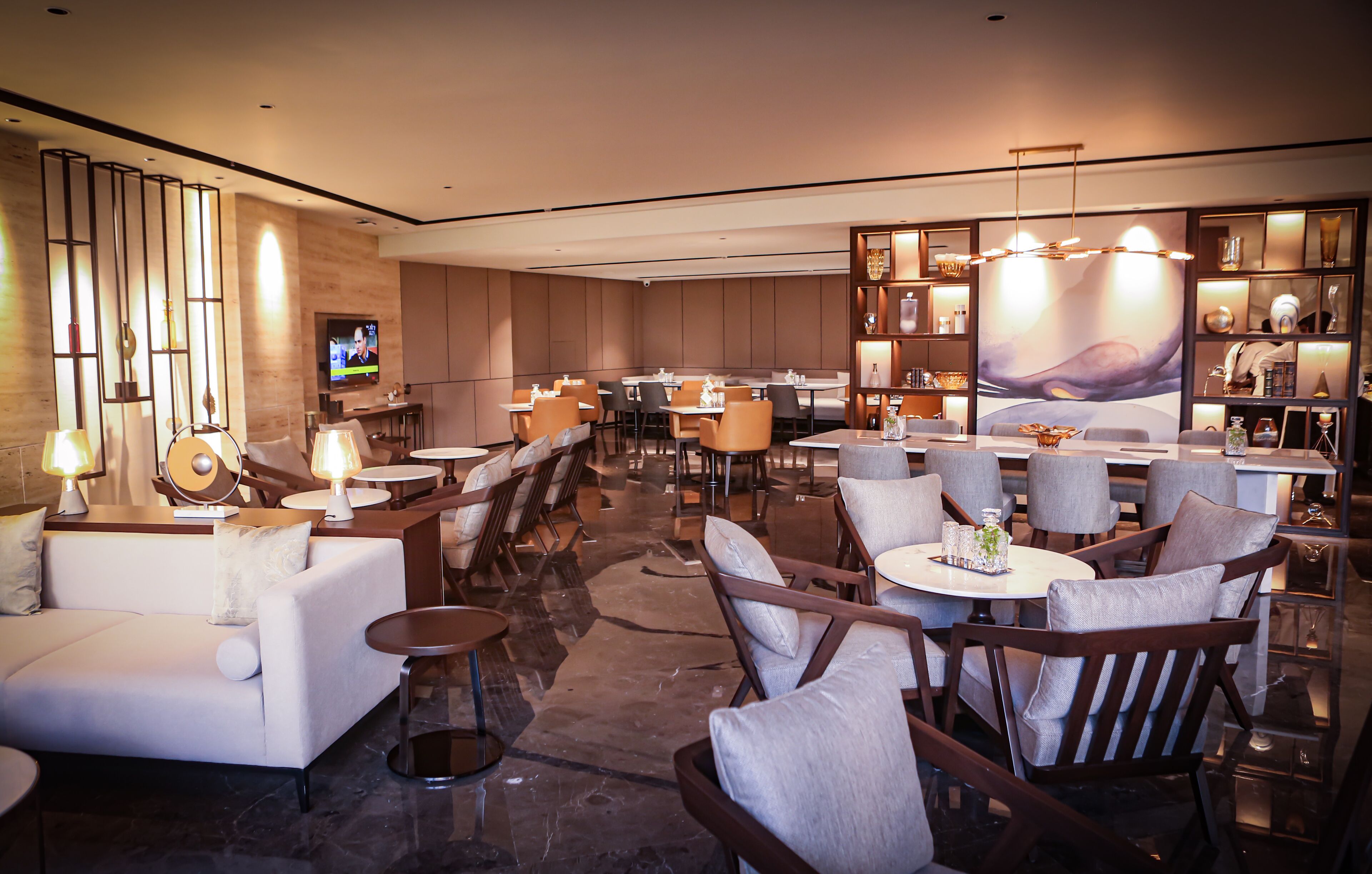 Um lobby de hotel moderno com diversas opções de assento, incluindo sofás e mesas redondas, além de um espaço de bar com televisão.