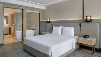 A modern hotel room with a large bed, bedside tables, a mirror, and a bathroom visible through an open door.