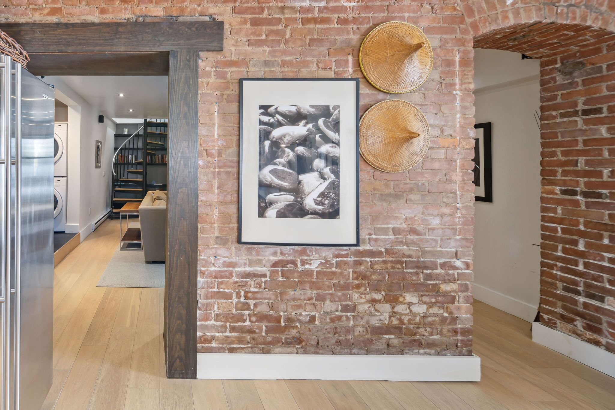 A brick wall with a framed photograph and two woven hats.
