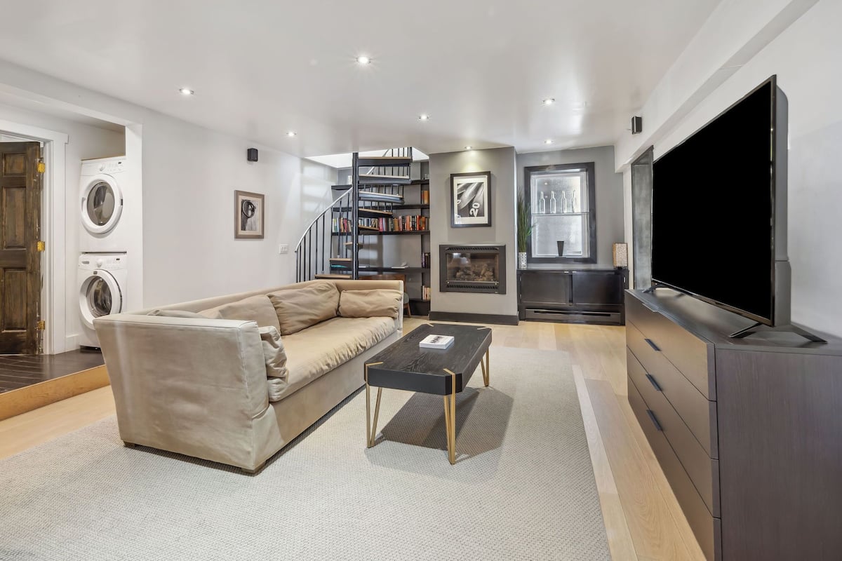 Un salon moderne avec un canapé beige, une table basse noire, un téléviseur à écran plat, une cheminée et un escalier menant à une mezzanine.