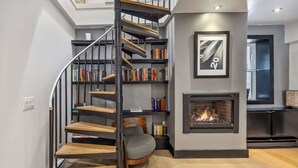A modern interior with a spiral staircase, a fireplace, and a bookshelf. - The Haus on Mirror Lake (Lake Placid)