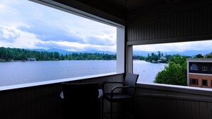 A room with a large window overlooking a lake, a chair, and a view of a building across the water.