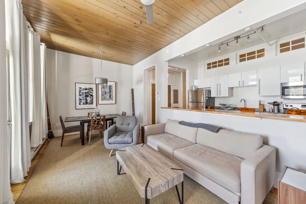 Un salon moderne avec un plafond en bois, un canapé, une table basse et un coin repas comprenant une table et des chaises.